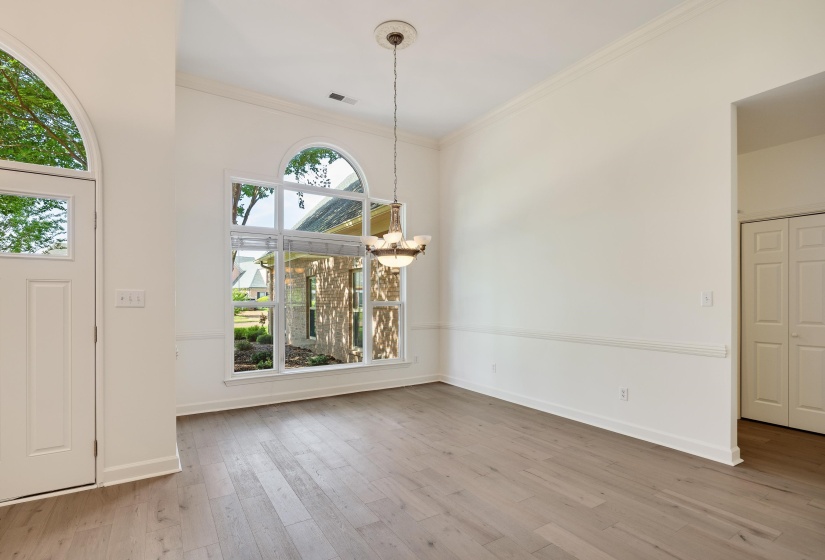 Spacious room featuring wood-finish flooring, a contemporary chandelier, and large windows with an arched transom