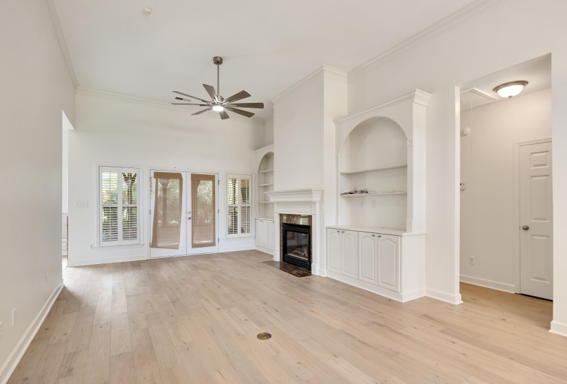 Spacious living area featuring light wood-finish flooring, a contemporary ceiling fan, and abundant natural light from multiple windows with plantation shutters