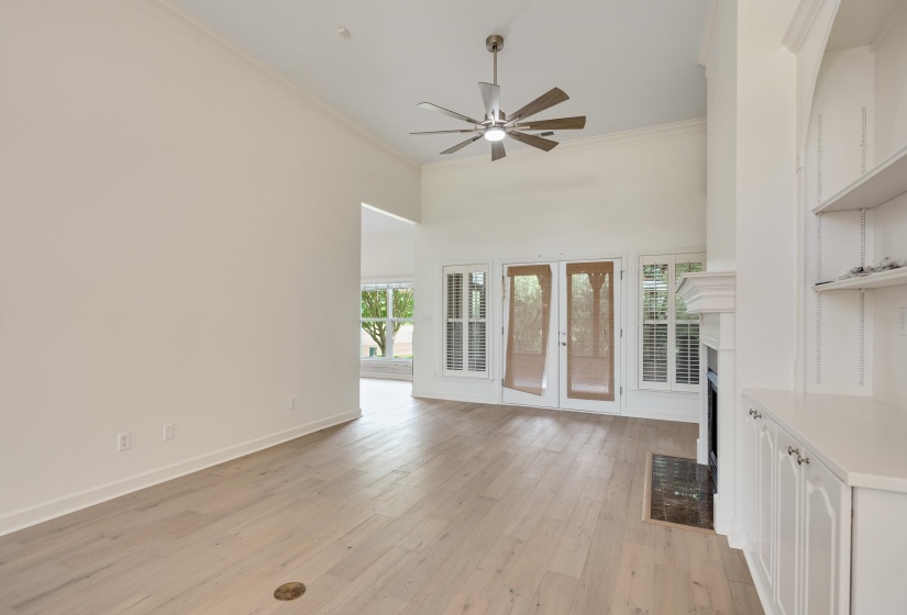 Spacious living area featuring light wood-finish flooring, a vaulted ceiling with a contemporary ceiling fan, and a fireplace with a dark tile hearth