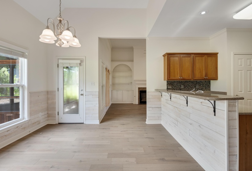 Open-concept living area featuring wood-finish flooring, a contemporary chandelier, a built-in wet bar with wood cabinetry and tile backsplash, and shiplap wall accents