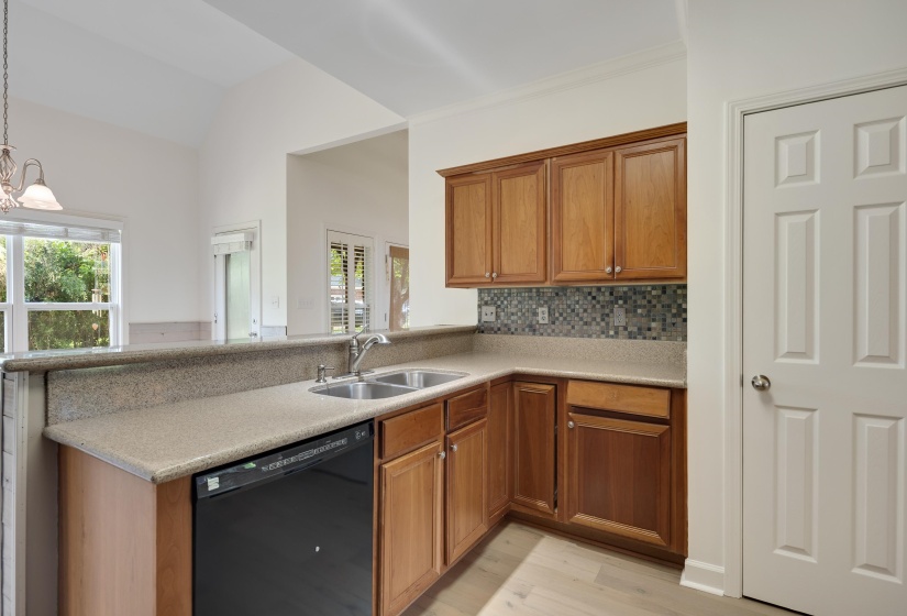 Kitchen featuring wood-finish cabinetry, a double basin stainless steel sink, black dishwasher, and a mosaic tile backsplash
