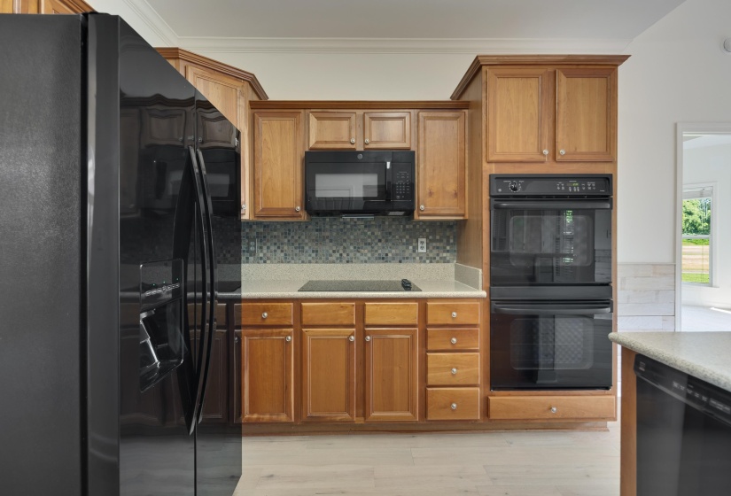 Kitchen featuring wood cabinetry, black appliances, a tile backsplash, light-toned countertops, and wood-finish flooring