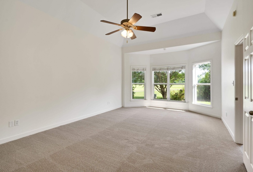 Spacious room featuring vaulted ceilings, a ceiling fan, light neutral-toned carpet, and a bay window configuration with three tall windows