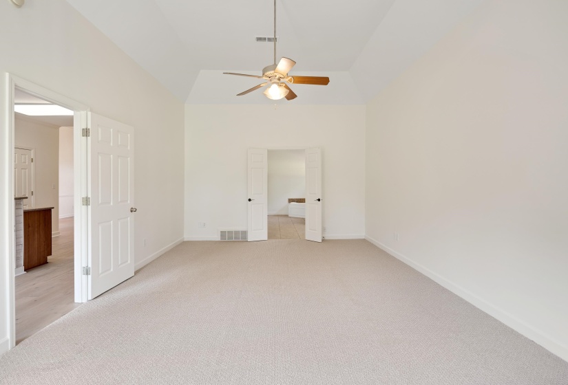 Spacious room featuring vaulted ceilings, a ceiling fan with light fixture, light-toned carpeting, and white paneled doors