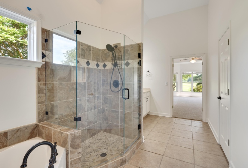 Glass-enclosed shower with tiled walls and floor, accompanied by a separate soaking tub with dark-finish fixtures