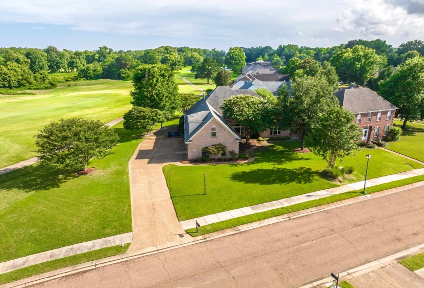 Brick exterior residence with a shingled roof, featuring a long driveway, a manicured lawn, and mature trees