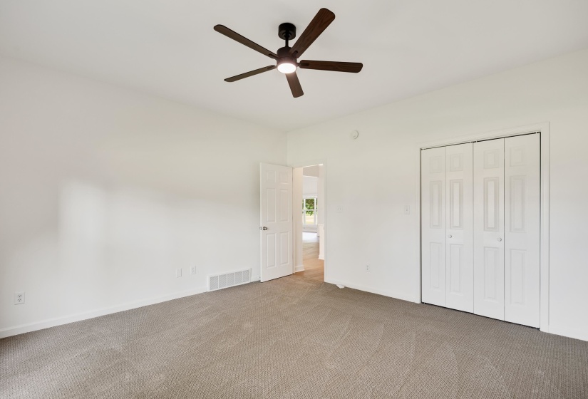 Spacious room featuring neutral carpeting, a ceiling fan with integrated lighting, a four-panel bi-fold closet, and white painted walls