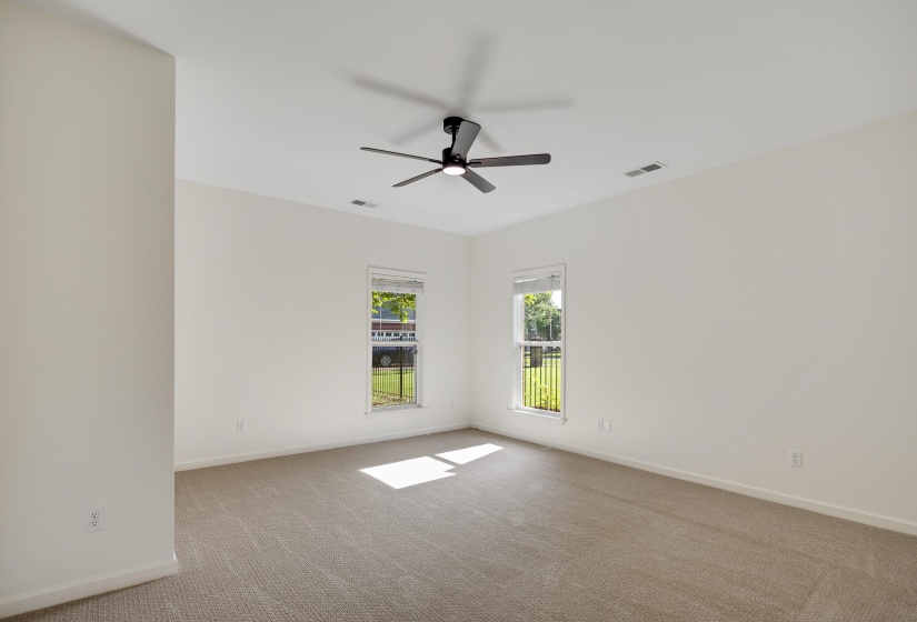 Spacious room featuring neutral carpet flooring, white walls, two windows with natural light, a ceiling fan, and white trim