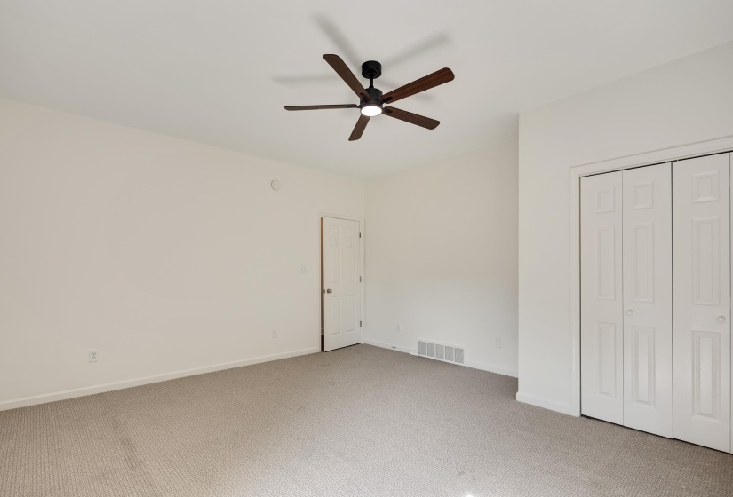 Expansive room featuring neutral-toned carpet, a ceiling fan with integrated lighting, and a double bi-fold closet