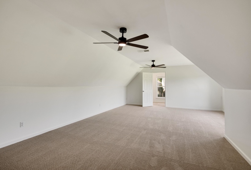 Spacious carpeted room featuring a white interior, sloped ceilings, and two ceiling fans with integrated lighting