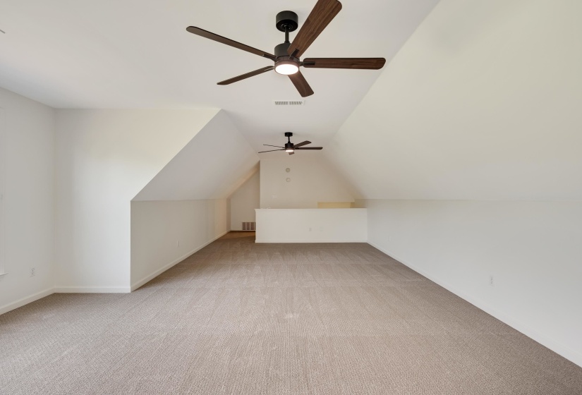 Spacious bonus room featuring sloped ceilings, plush carpeting, and two ceiling fans with integrated lighting