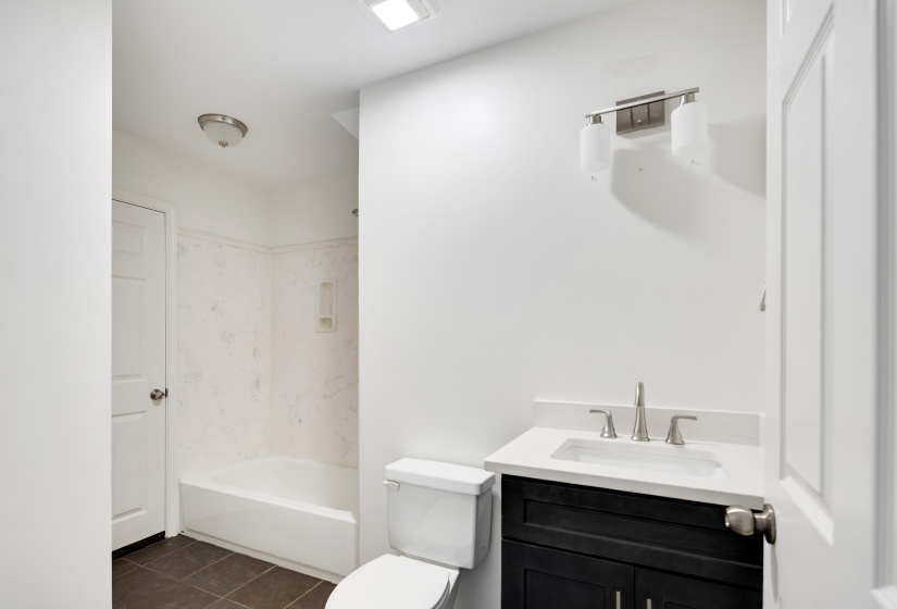 Bathroom featuring a white bathtub with a shower surround, dark floor tiling, and a vanity with a white countertop and dark cabinetry