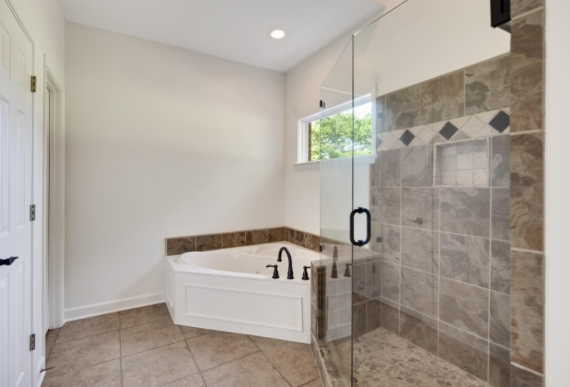 Shower with clear glass enclosure and a built-in corner tub featuring a tiled surround