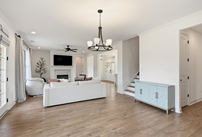 Living room with a ceiling fan, a chandelier, light wood finished floors, a fireplace, and crown molding