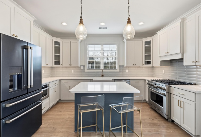 Kitchen featuring high quality fridge, glass insert cabinets, a kitchen island, stainless steel gas stove, and pendant lighting