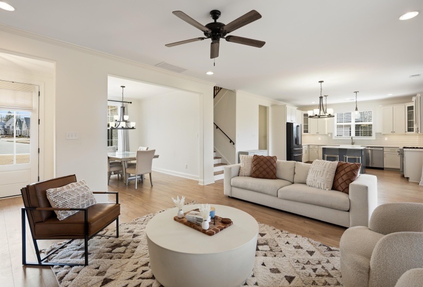Living room with suspended lighting, ceiling fan, light wood-style floors, and crown molding