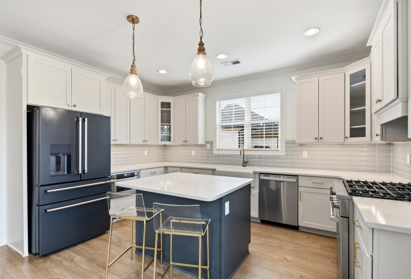 Two tone kitchen with glass fronted cabinets, stainless steel appliances, light wood-style floors, pendant lighting, and two tone cabinets