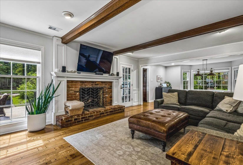 Living area featuring a brick fireplace with a white mantel, exposed ceiling beams, wood-finish flooring, and French doors
