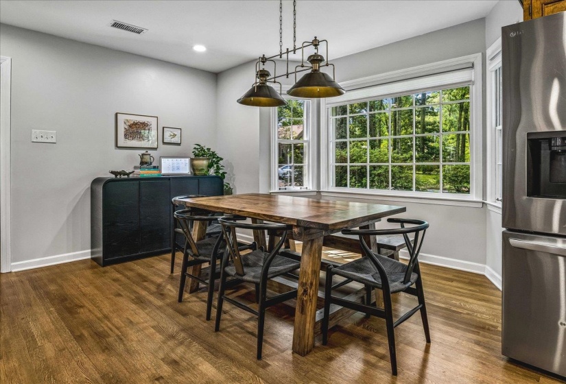 Dining area featuring a bay window with grid-patterned panes, wood-finish flooring, recessed lighting, a built-in industrial-style chandelier (does NOT sell with listing), and a stainless steel refrigerator