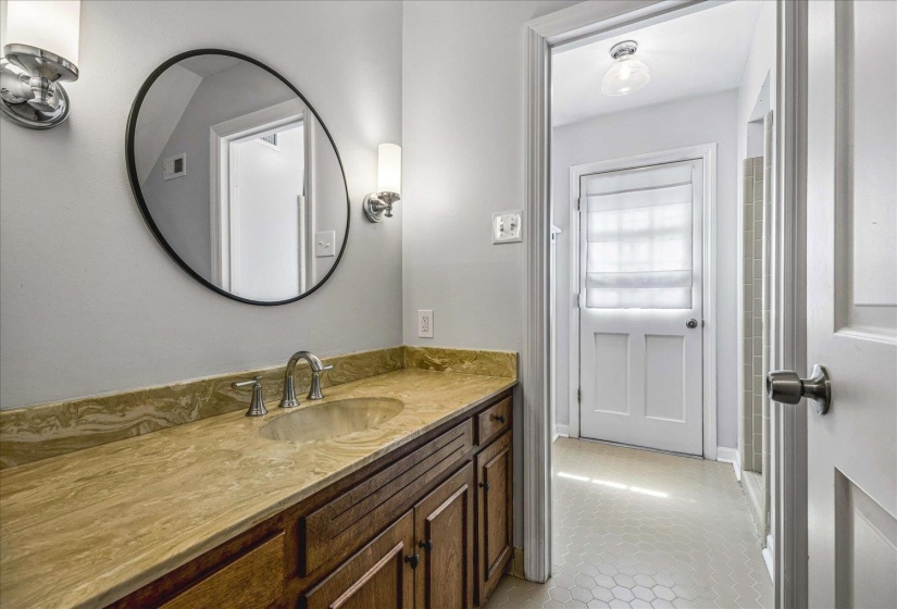Bathroom vanity featuring a stone countertop with an integrated sink, wood-finish cabinetry, and a circular mirror