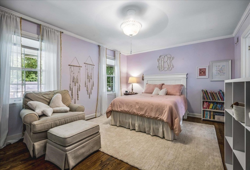 Bedroom featuring wood-finish flooring, a white paneled headboard, and dual windows with natural light