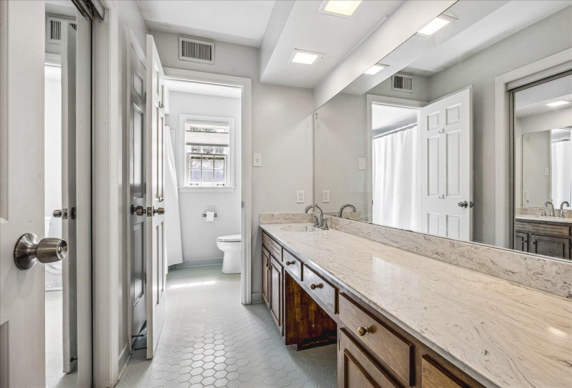Bathroom featuring a dual-sink vanity with a stone countertop, wood cabinetry, and a full-width mirror