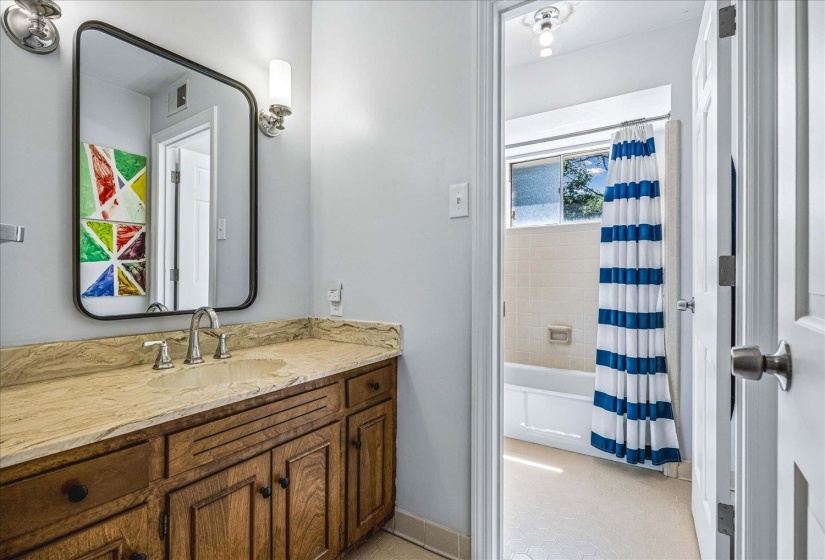 Bathroom vanity featuring a natural stone countertop, undermount sink, and wood cabinetry with dark hardware