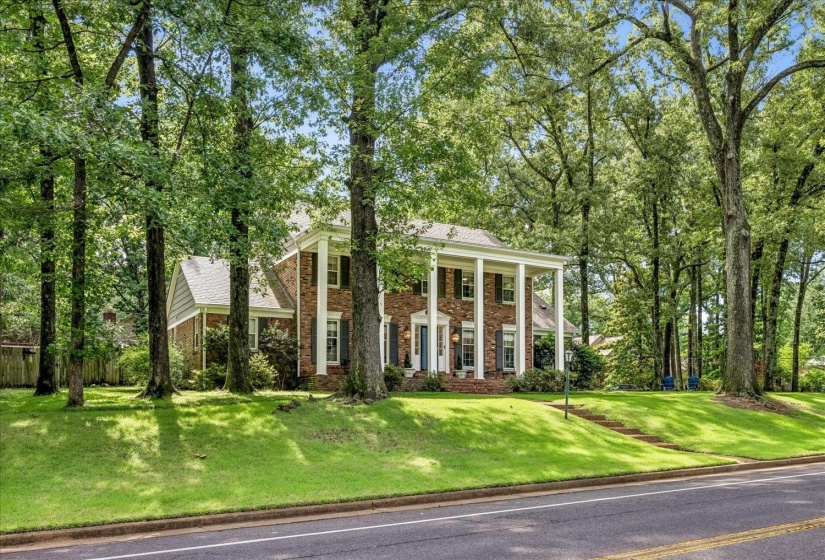 Brick Colonial-style residence featuring a portico with white columns, dark shutters, and a prominent front door