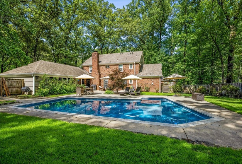 Expansive inground swimming pool with surrounding concrete patio and well-maintained lawn