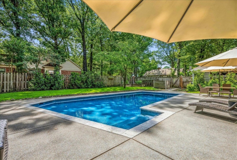 In-ground swimming pool with a concrete patio surround, surrounded by mature trees and a wooden fence