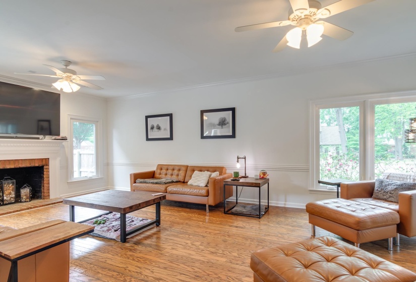 Spacious living area featuring wood-finish flooring, a brick fireplace with a white mantel, and multiple large windows