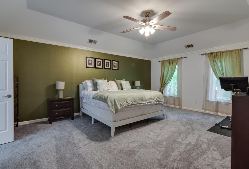 Spacious bedroom featuring neutral carpeting, a tray ceiling, and a ceiling fan with integrated lighting