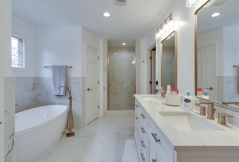 Bright bathroom featuring a freestanding tub with a floor-mounted faucet, a double vanity with undermount sinks and quartz countertops, and a glass-enclosed shower