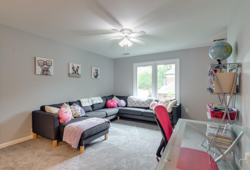 Spacious room featuring light gray walls, plush gray carpeting, and a white ceiling fan