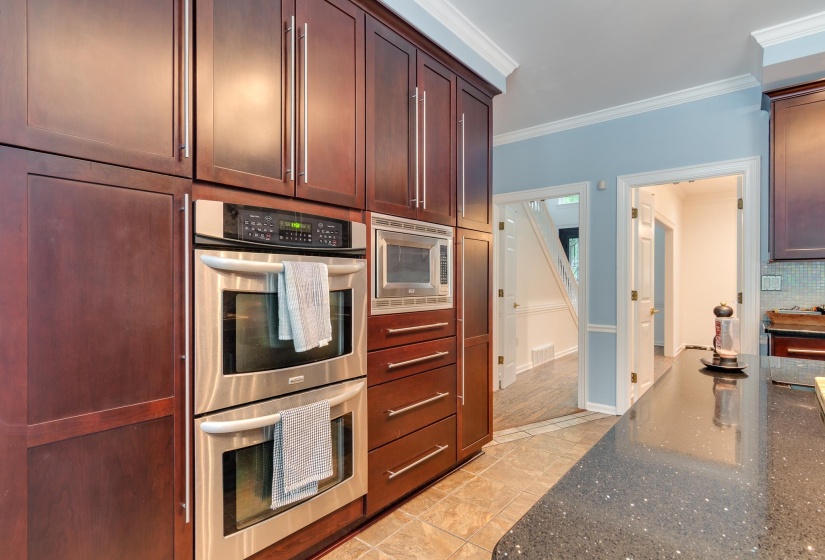 Kitchen featuring dark wood cabinetry, stainless steel double wall ovens, a built-in microwave, and a dark speckled countertop