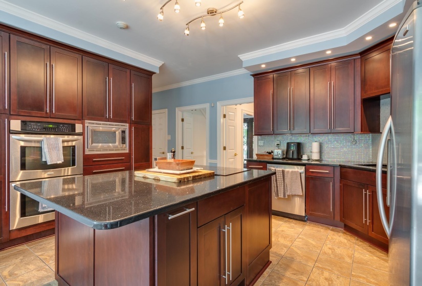Kitchen featuring an island with a dark countertop, extensive dark wood cabinetry, integrated stainless steel appliances, a light blue wall color, and tiled flooring