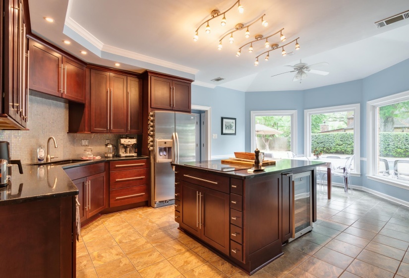 Kitchen featuring rich wood cabinetry, stainless steel appliances, a central island with integrated beverage cooler, tile flooring, and multiple windows