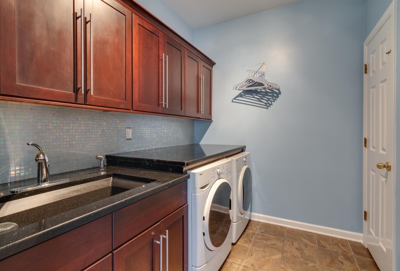 Laundry area featuring dark wood-finish cabinetry, a dark countertop with an integrated sink, and a mosaic tile backsplash