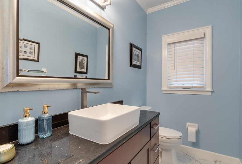 Bathroom featuring a rectangular vessel sink, brushed nickel single-handle faucet, dark wood-finish vanity with drawer storage, and a black speckled countertop