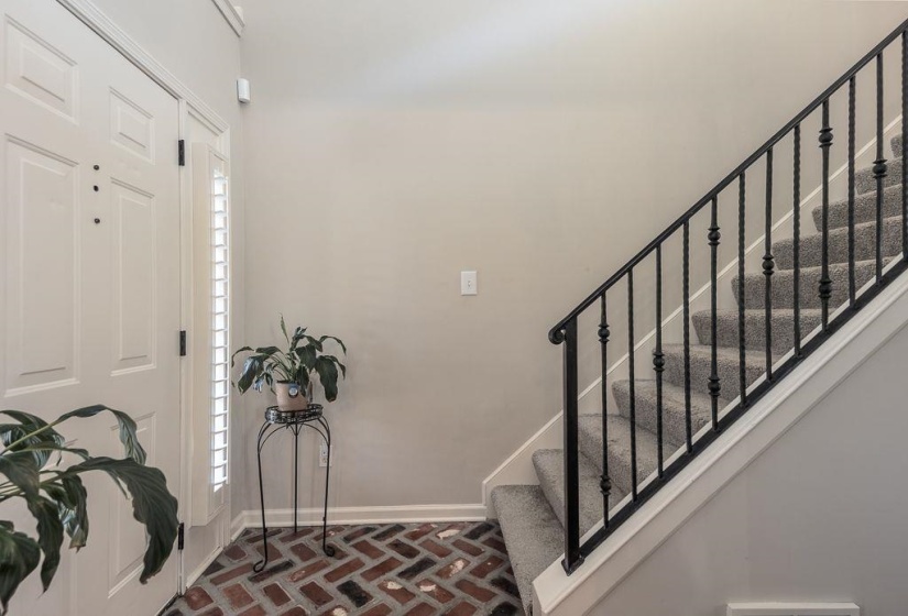 Entryway featuring a white paneled door, brick-patterned flooring, and a carpeted staircase with wrought iron balusters