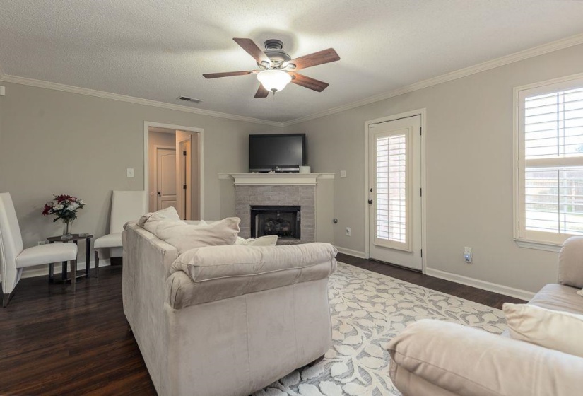 Living area featuring wood-finish flooring, a fireplace with a stone surround and mantel, and crown molding