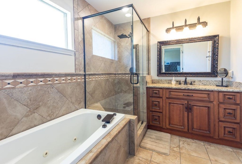 Bathroom featuring a jetted tub, glass-enclosed shower, wood vanity with granite countertop, and decorative wall tiling