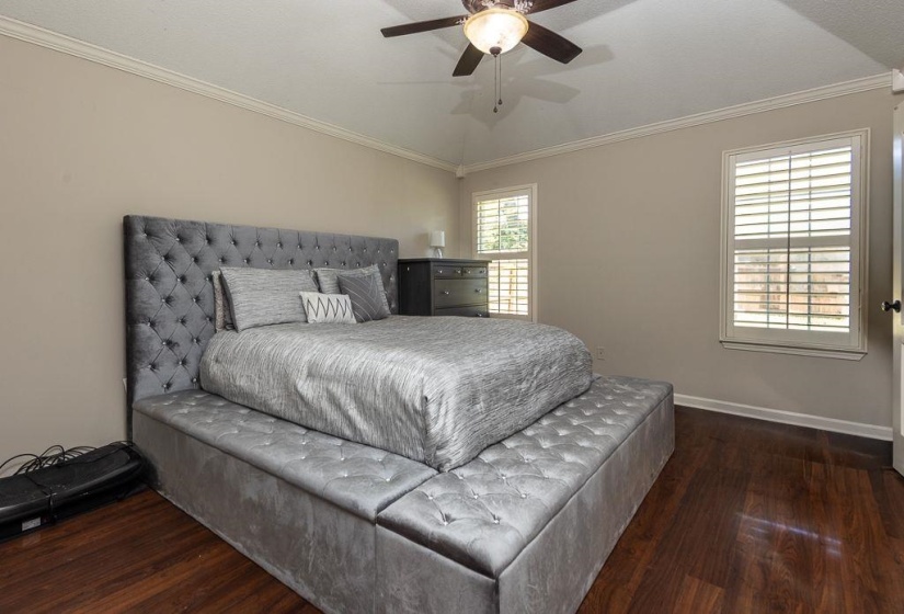 Room featuring rich wood-finish flooring, crown molding, and two windows with white plantation shutters