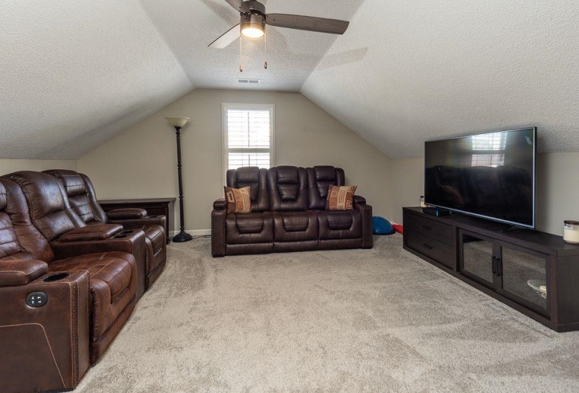 Carpeted bonus room featuring a window with plantation shutters, sloped ceilings, and a ceiling fan with integrated lighting