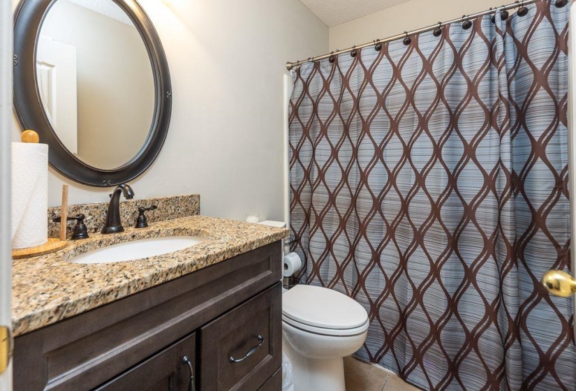 Vanity with an oval mirror, granite countertop, undermount sink, and dark wood-finish cabinetry