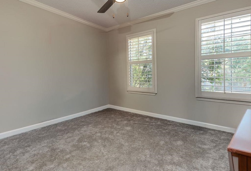 Interior room featuring two windows with white plantation shutters, gray carpet flooring, light gray wall paint, white baseboards, and crown molding
