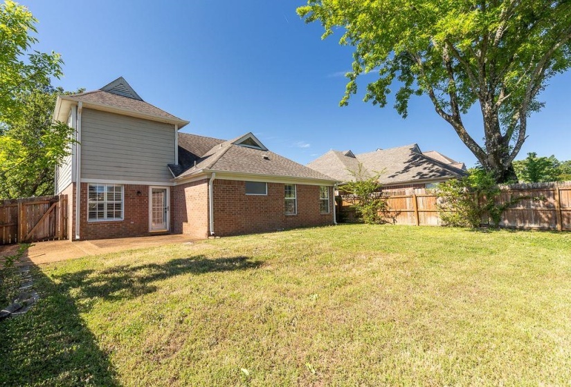 Spacious rear yard featuring an expansive grassy area, mature trees, and a wooden privacy fence