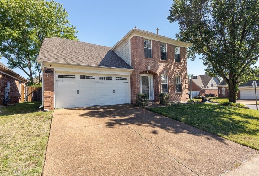 Brick facade residence featuring a two-car garage with panel doors, a concrete driveway, and established landscaping