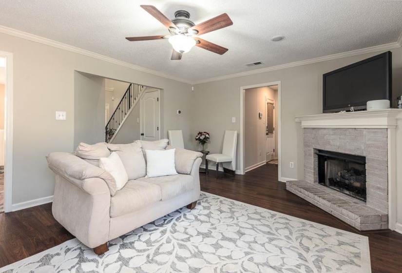 Living room featuring dark wood-finish flooring, a ceiling fan with integrated lighting, and crown molding