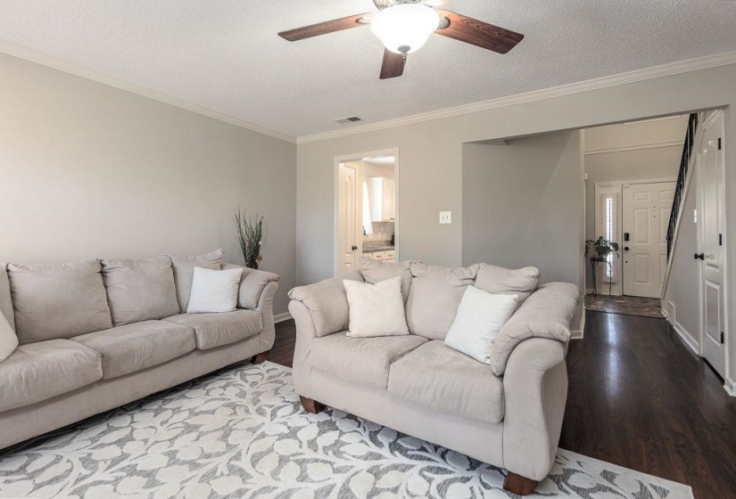 Living area with dark wood-finish flooring, light-toned walls, and a ceiling fan with integrated lighting